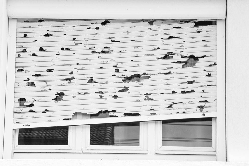 durch hagelschaden zerstörter Rollladen vor Fenster